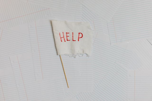 A fabric flag with 'HELP' on a scattered notepaper background, symbolizing distress or overwhelm.